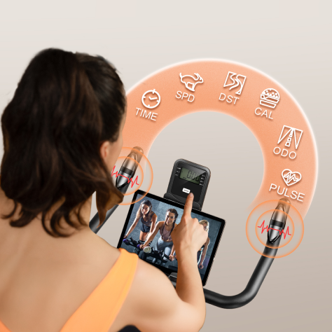 A woman cycling on an exercise bike, with the digital display showing her real-time workout metrics including speed, distance, and heart rate.