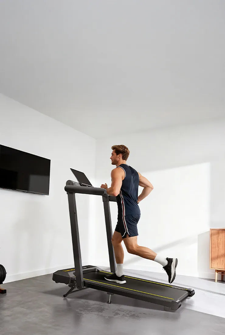 Person using a TP5 treadmill in a modern room with a TV on the wall.