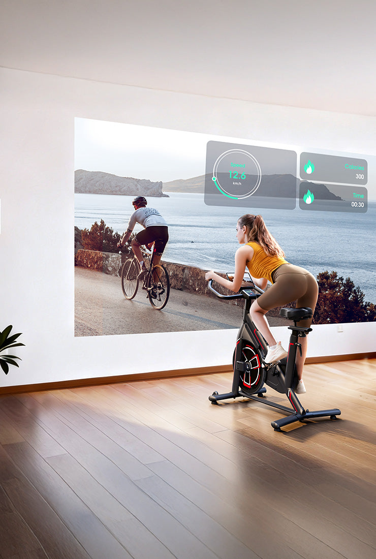  A woman cycling on an exercise bike at home, fully immersed in a virtual landscape projected by an app onto a large screen for dynamic indoor training.