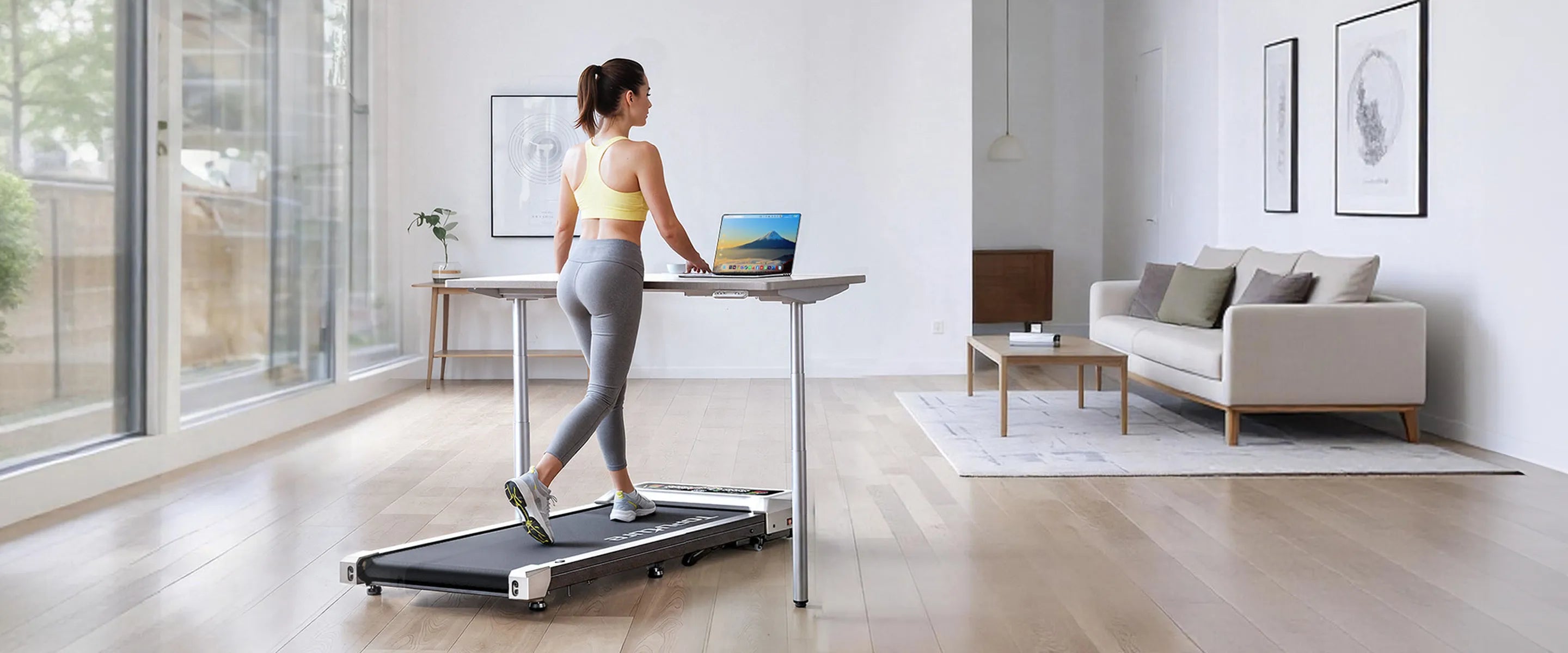 A woman walking on a TP8 under‑desk walking pad while working on her computer, seamlessly blending movement with productivity at home.
